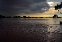 “Dark storm clouds gathering over Indus River with water level rising in nearby fields”