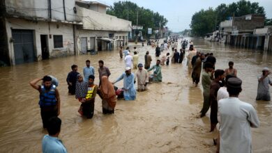 Villagers wade through floodwaters with belongings, showing the severity of the monsoon floods.